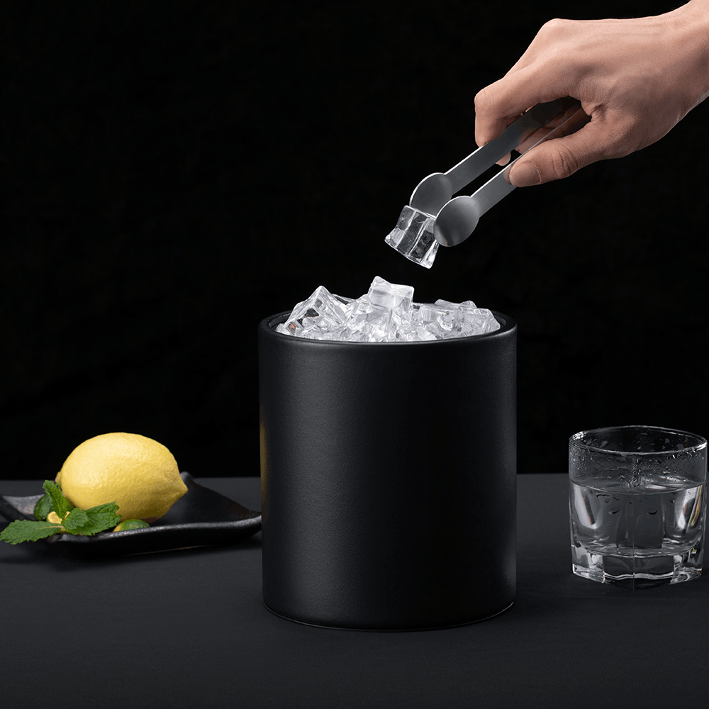 Hand using ice tongs to lift a cube from the Black SLUSH leatherette ice bucket